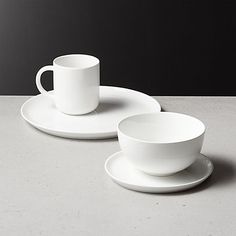 two white cups and saucers sitting on top of a table next to each other