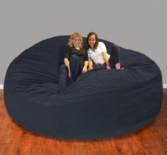 two women sitting on a bean bag chair in the middle of a hardwood floored room