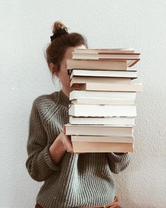 a woman holding a stack of books in front of her face while wearing a sweater