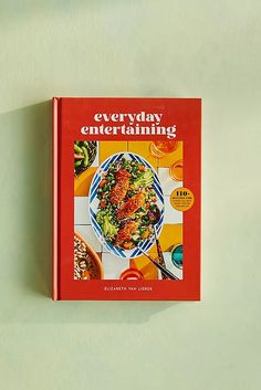 a cookbook with an image of a bowl of food on the front cover, sitting against a green wall