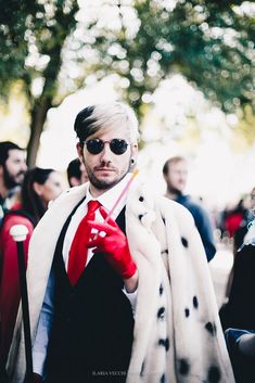 a man with white hair and sunglasses wearing a red tie, black vest and polka dot scarf