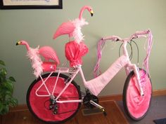 a pink bicycle decorated with flamingos on the front and rear wheels, sitting on a wooden floor