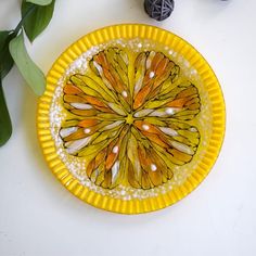 a yellow plate with an orange and white butterfly on it next to some green leaves