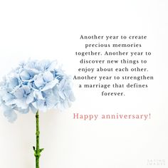 a blue flower sitting on top of a table next to a happy anniversary card with the words, another year to create precious memories together