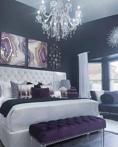 a white bed sitting in a bedroom next to a purple chair and chandelier