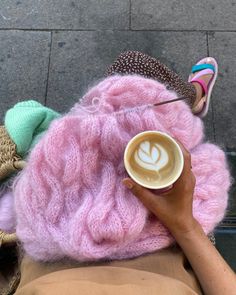 a person is holding a cup of coffee in their hand while sitting on the ground