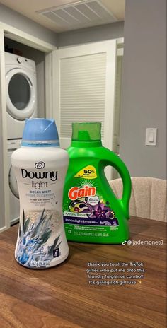 two bottles of detergent sitting on top of a wooden table next to a washing machine