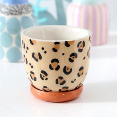 two coffee cups sitting next to each other on top of a white table with colorful vases in the background