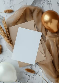 an envelope, gold balloon and other items on a marble surface with white paper in the middle