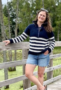 a woman standing on a wooden bridge posing for the camera with her hands in her pockets