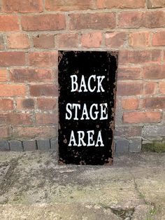 a black sign that says back stage area on the side of a bricked building