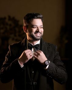 a man in a tuxedo adjusts his tie while smiling at the camera