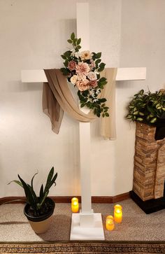 a cross with flowers and candles in front of it on the floor next to a potted plant