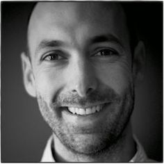 a black and white photo of a man with a bald head smiling at the camera