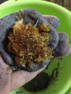 a hand holding up a piece of food in a green bowl on top of a wooden table