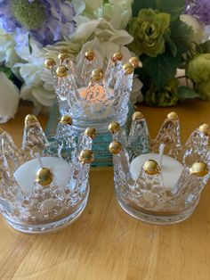 two clear glass candlesticks sitting on top of a wooden table next to flowers