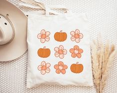 a white bag with orange flowers and pumpkins on it next to a straw hat