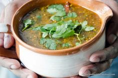 a person holding a bowl of soup with cilantro and coriant leaves