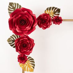 red paper flowers with gold leaves are on a white surface, next to a golden stick