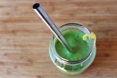 a glass filled with green liquid on top of a wooden table next to a spoon