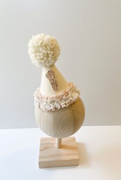 a white hat on top of a wooden stand with a pom - pom