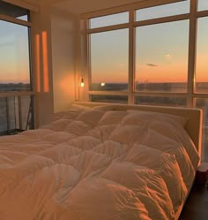 an unmade bed sitting in front of two large windows