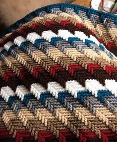 a crocheted blanket is sitting on a table next to a cup and pen