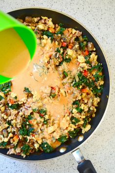 a pan filled with vegetables and sauce being poured on top of the food in it