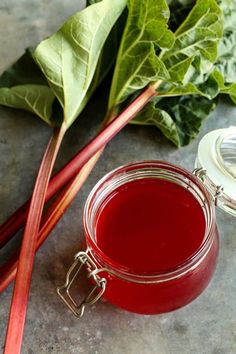 a glass jar filled with red liquid next to some green leafy vegetables on a table