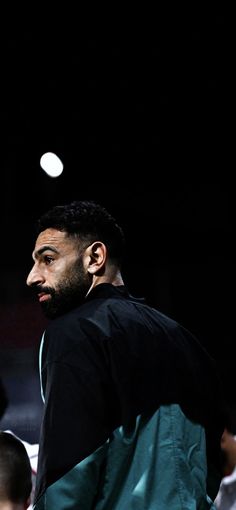 a man with a beard standing in front of a crowd at a basketball game and looking off into the distance