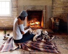 a woman sitting in front of a fireplace with her dog