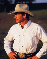 a man in a white shirt and cowboy hat standing with his hands on his hips