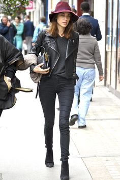 a woman walking down the street wearing a hat and carrying a purse in her hand