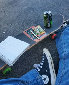 a person sitting on the ground next to a skateboard and a can of soda