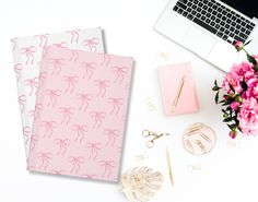 two notebooks with pink bows on them next to flowers and a laptop computer sitting on a desk