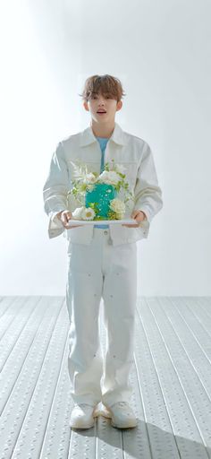 a boy in white holding a cake with blue frosting and flowers on the plate