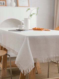 a white table cloth with tassels and a coffee cup on the top is sitting on a wooden chair