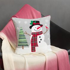 a snowman pillow sitting on top of a chair next to a blanket and a christmas tree