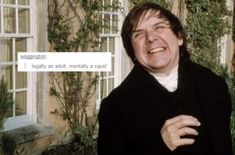 a man is laughing while standing in front of a building with ivy growing on it