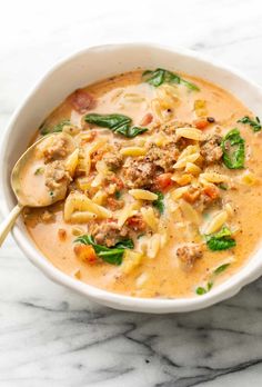 a white bowl filled with pasta, meat and spinach soup on top of a marble counter