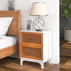 a nightstand with a lamp on top of it next to a bed and potted plant