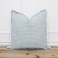 a light blue pillow sitting on top of a wooden floor next to a white wall