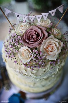 a cake with flowers and bunting on the top is decorated in pink, purple and white