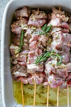 meat skewers in a white casserole dish with olives and rosemary