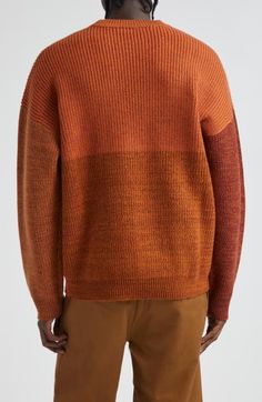 a man wearing an orange sweater and brown pants with his back turned to the camera