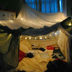 an unmade bed with white sheets and string lights on the ceiling, in front of a window