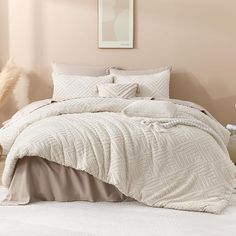 a bed with white comforter and pillows in a room next to a plant on the floor