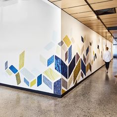 a man walking down a hallway next to a white wall with colorful designs on it