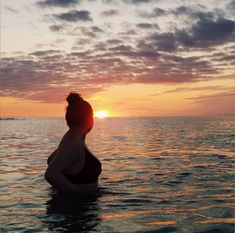 a pregnant woman sitting in the water at sunset with her head back to the camera