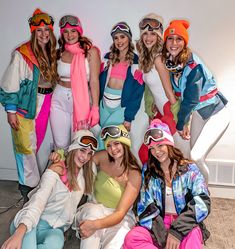 a group of women wearing ski goggles pose for a photo in front of a white wall